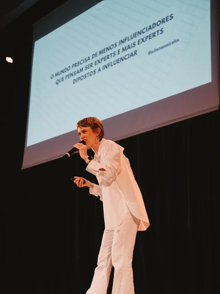Mari Krüger de terno branco palestrando com telão ao fundo