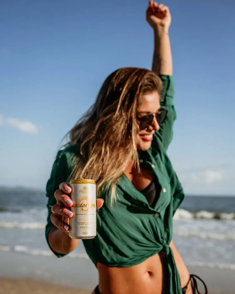Mulher na praia com lata de bebida saudável e refrescante.