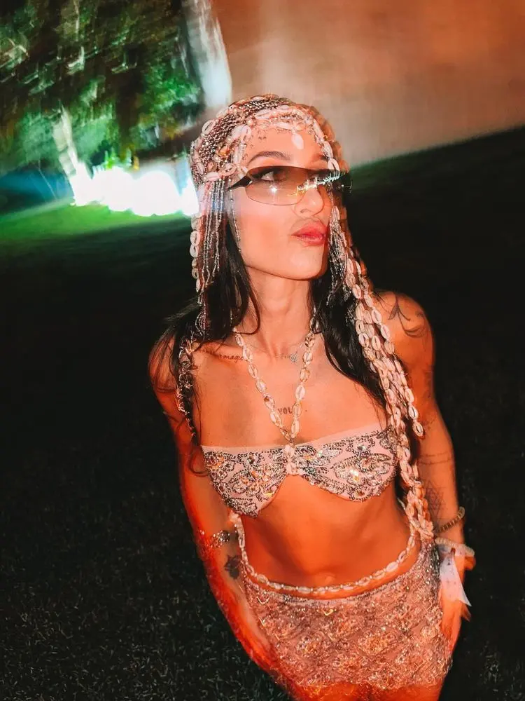 Mulher de pele clara com top e saia de miçangas, além de acessório no cabelo feito com búzios