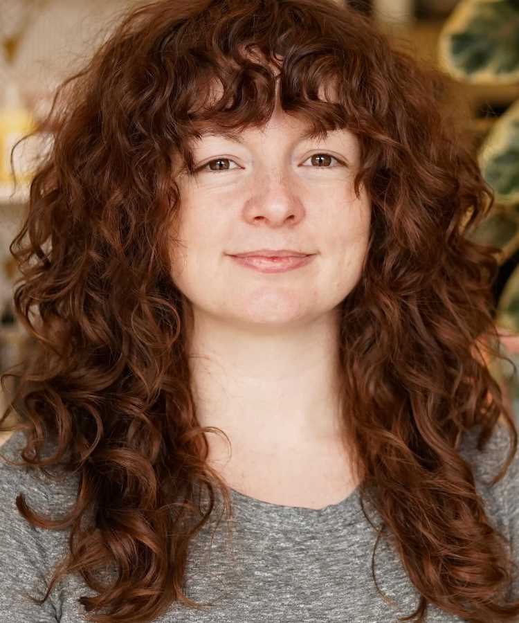 A imagem mostra uma pessoa com cabelo cacheado e volumoso, cortado em camadas repicadas. O corte ajuda a definir os cachos e distribuir o volume de forma equilibrada. A franja é curta e também repicada, adicionando um toque moderno ao visual. Esse estilo é frequentemente chamado de "corte em camadas repicadas" para cabelos cacheados.


