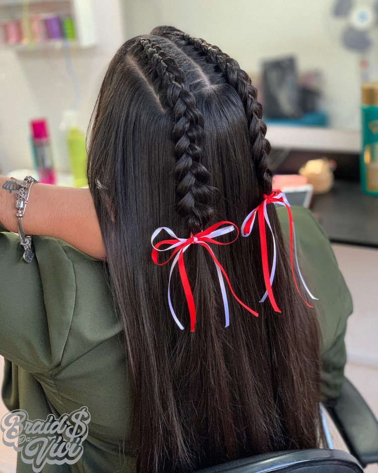 duas tranças embutidas em cabelo preto amarradas com fitas vermelha e branca.