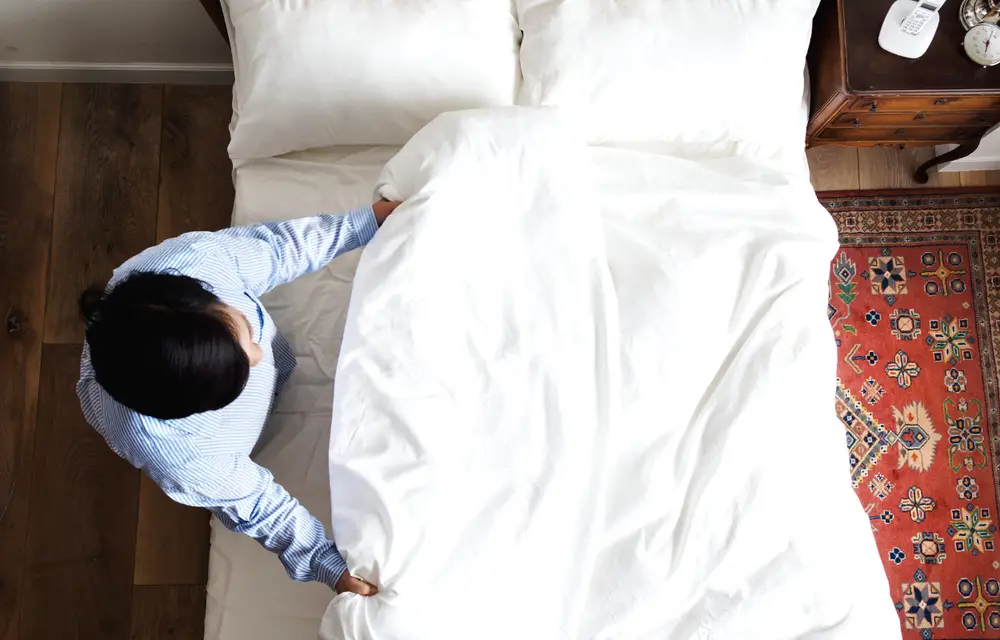 Imagem de uma mulher arrumando sua cama para dormir melhor.