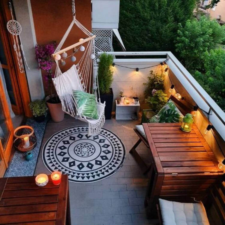 Varanda decorada com plantas, almofadas, tapete, mesas de madeira e fios com lâmpadas