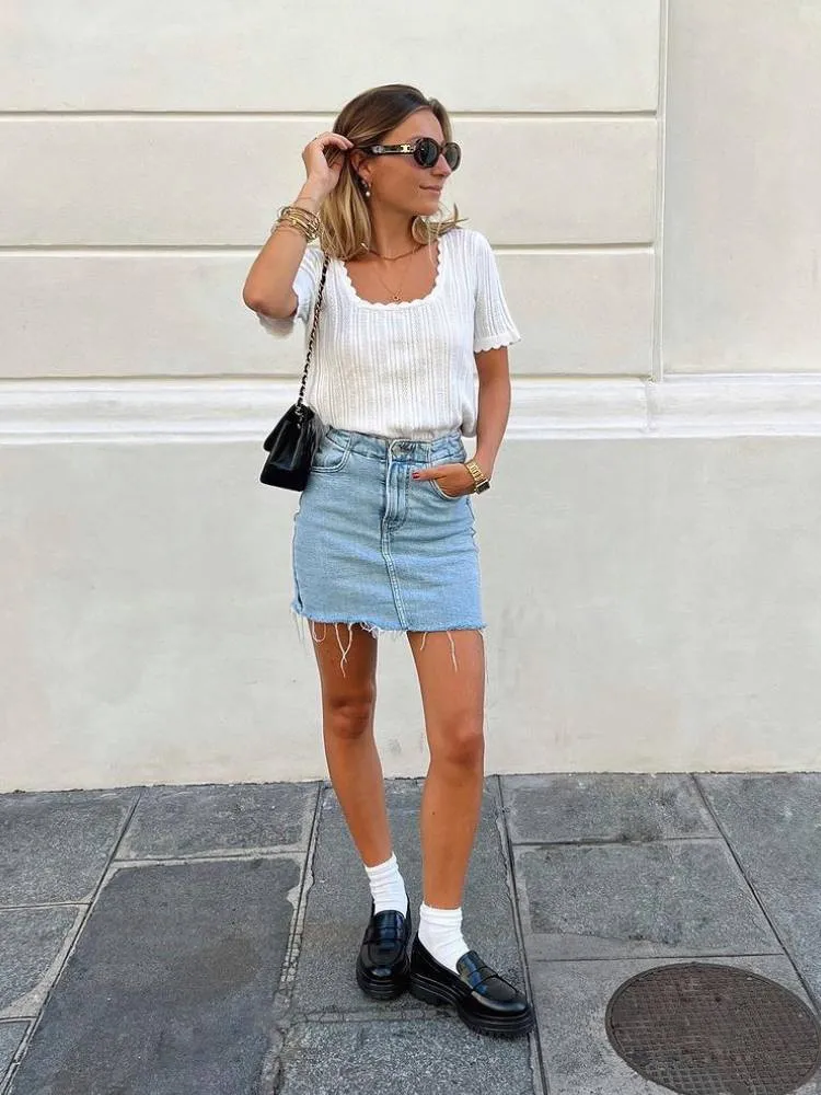 mulher usando camiseta branca, saia jeans, meia branca e mocassim preto tratorado