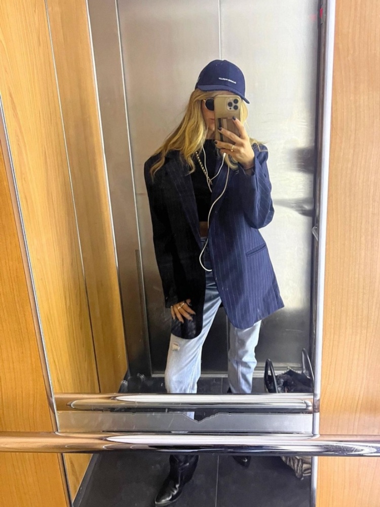 mulher usando blazer de risca de giz azul com calça jeans, blusa preta, boné azul e bota preta