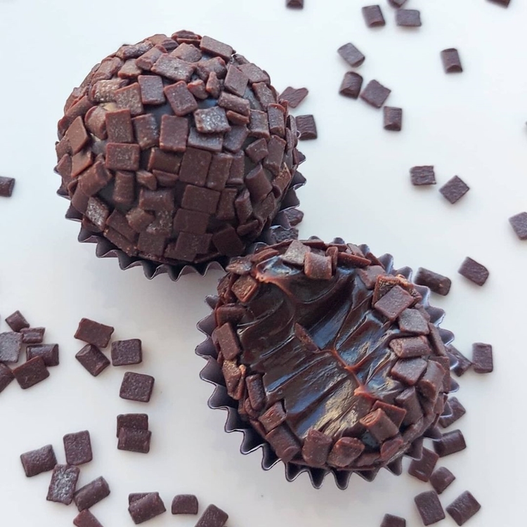 Foto de dois brigadeiros com granulados e na forma, sendo um deles mordido