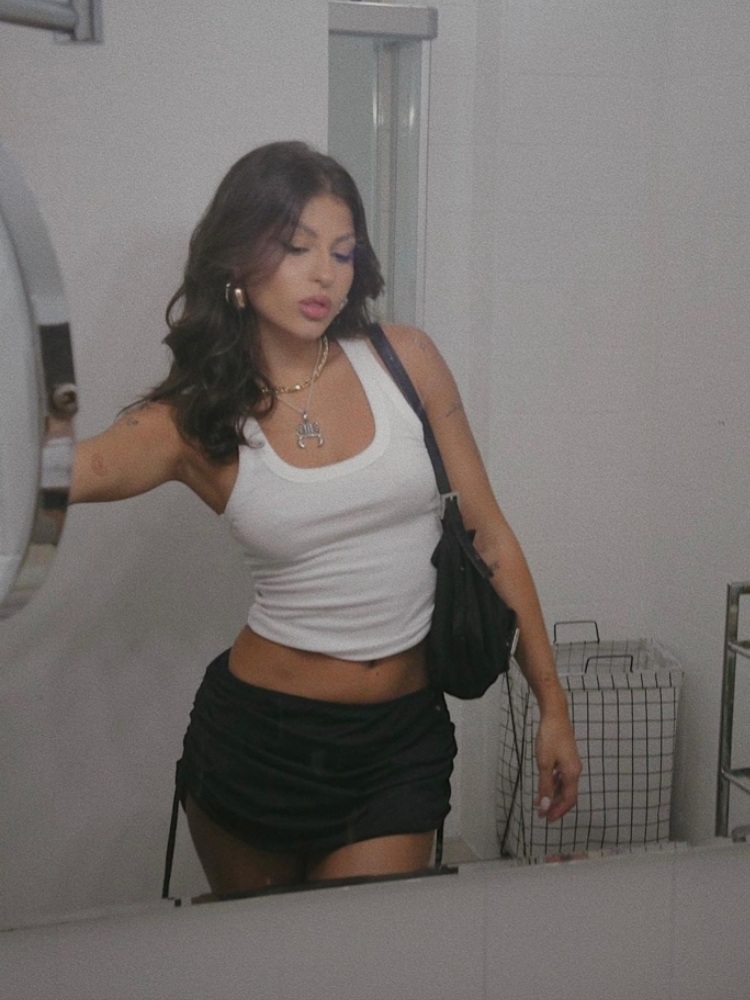 mulher usando regata branca com mini saia preta e bolsa de ombro