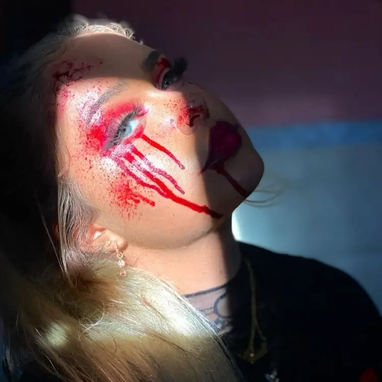 Foto de mulher loira de olhos verdes com maquiagem de Halloween com sangue de mentira