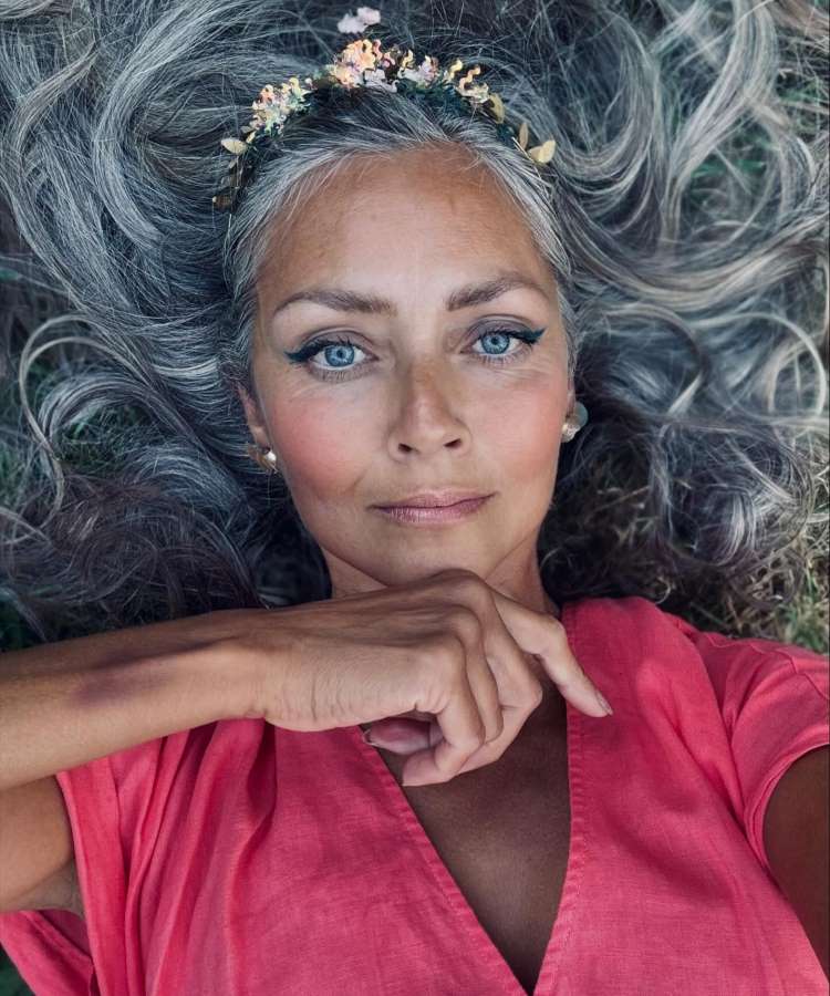 Mulher madura com roupa rosa, tm cabelos brancos e usa tiara de flores