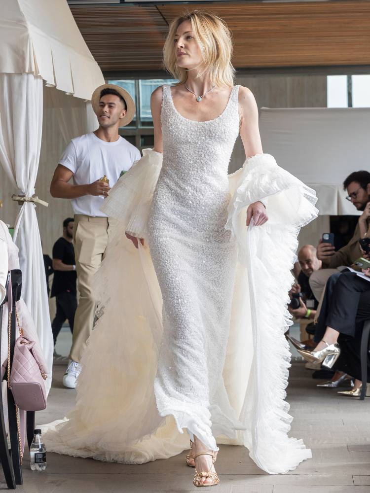 Mulher de pele clara desfilando com vestido de noiva bordado e casaco branco
