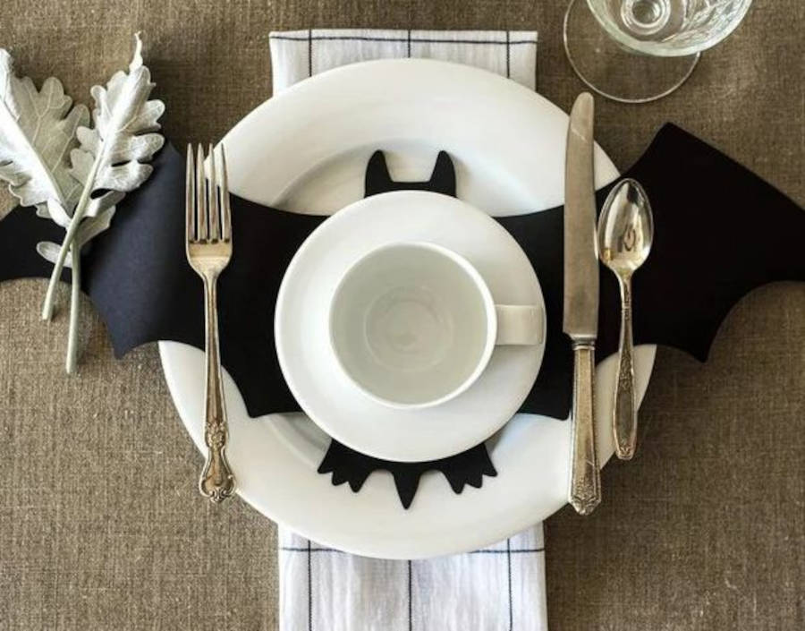 Mesa posta com pratos brancos e morcego de papel sobre eles