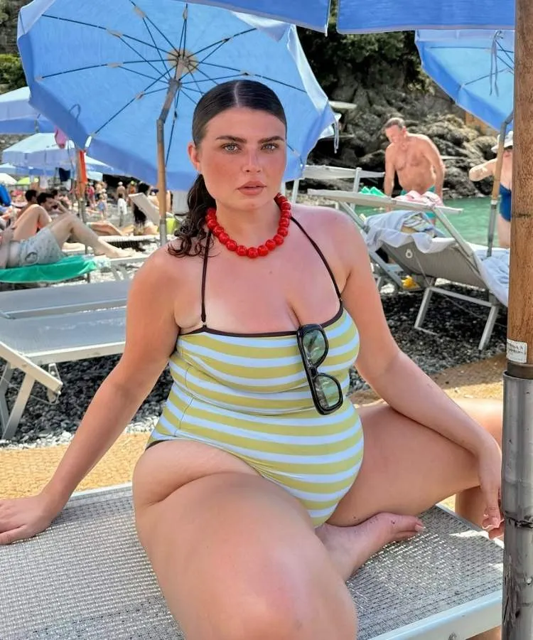 Mulher em cadeira de praia embaixo de guarda-sol azul usando maiô listrado amarelo e branco com detalhes em preto
