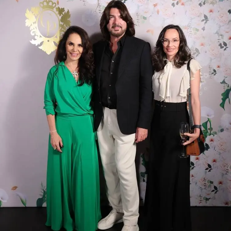 Cris Porto de verde, Stephane Rolland de terno preto e calça off-white e Denise Pitta de branco e preto em fundo com papel de parede com logo da Cris Porto joalheria e flores