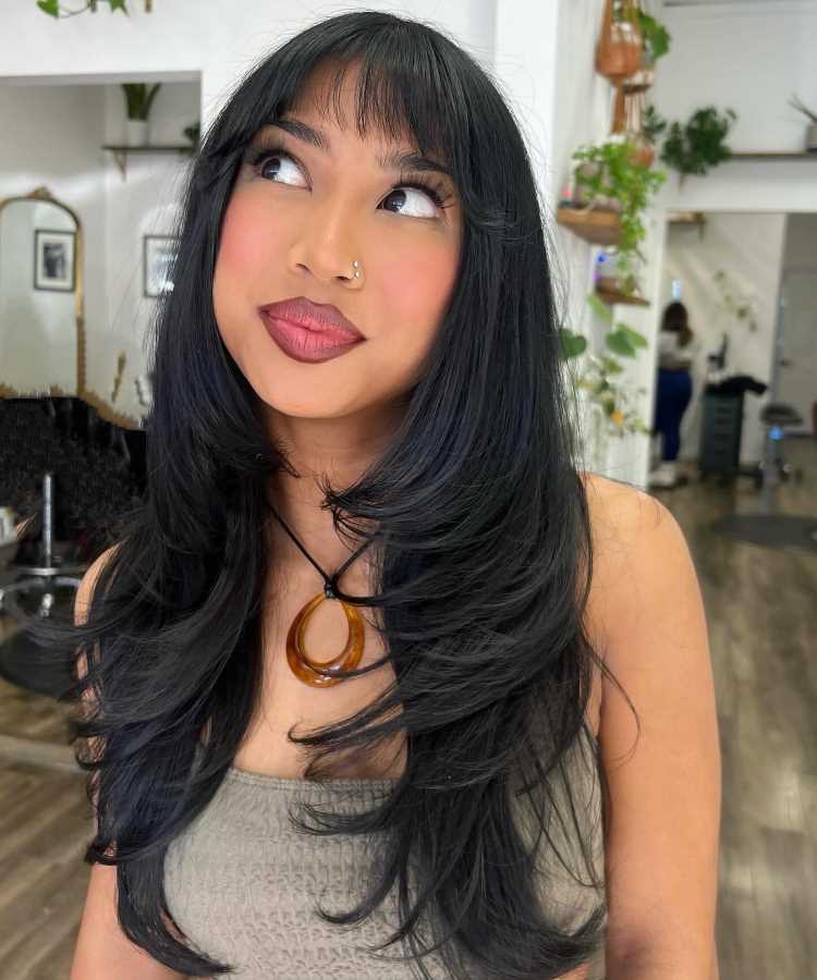 A imagem mostra uma pessoa com um corte de cabelo longo e repicado, com camadas que criam movimento e volume. A franja é reta e levemente desfiada, complementando o estilo. Esse tipo de corte é frequentemente chamado de "corte em camadas" ou "corte repicado", que é popular por sua versatilidade e por adicionar textura ao cabelo.


