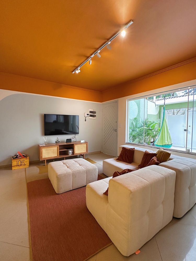 Sala de estar com teto laranja, parede branca e azul, estofados beges e decorações em marrom