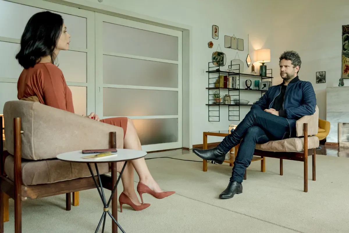 Cena de conversa intensa em série dramática do Globoplay ambientada em sala moderna durante sessão de entrevista.