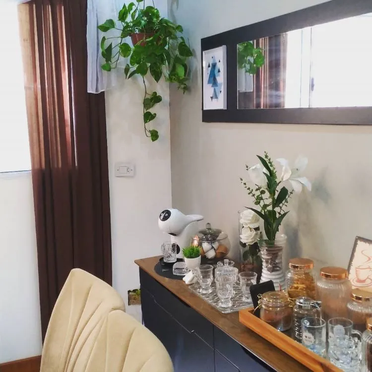 Parte de uma sala com aparador, espelho, poltrona, cortina marrom e vaso pendente de jiboia.