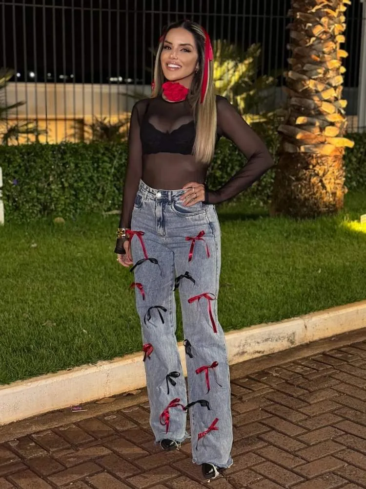 Mulher de pele clara usando body preto de tule com top e calça jeans com laços de fita
