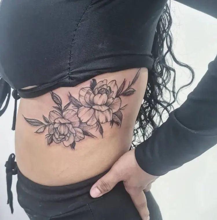 Tatuagem grande de flor na costela de mulher com roupas pretas