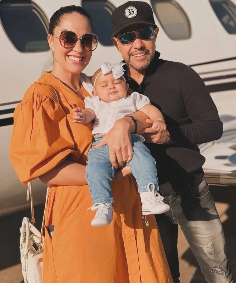 Casais famosos que reataram: Zezé Di Camargo e Graciele Lacerda posam com uma criança pequena, que parece estar dormindo tranquilamente nos braços de Graciele, ao lado de um avião particular. A família sorri, transmitindo uma atmosfera de felicidade.

