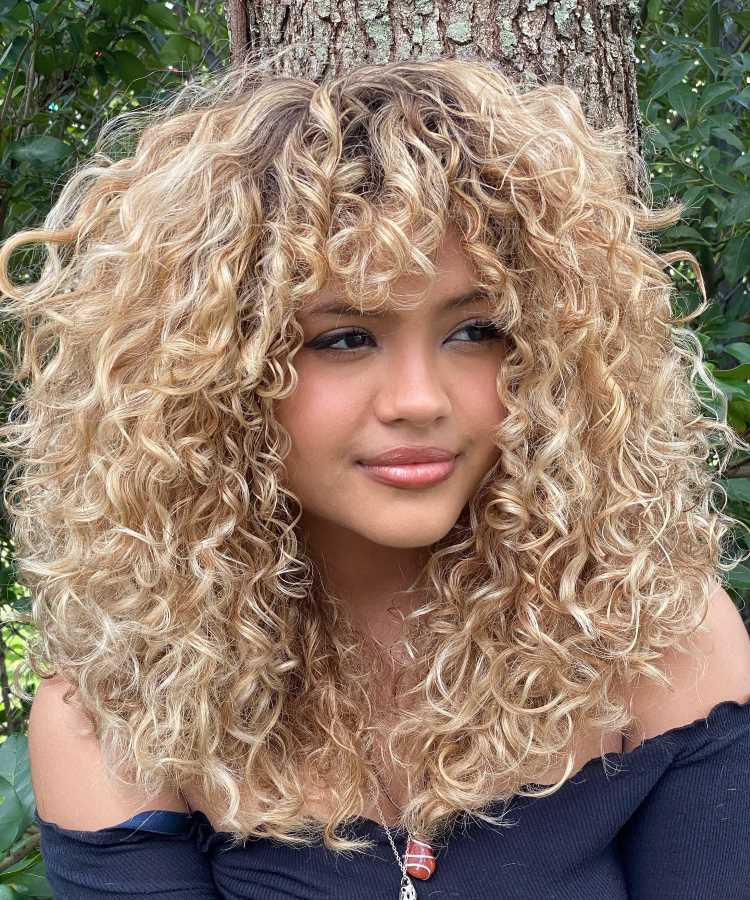 A imagem mostra uma pessoa com cabelo cacheado e volumoso, cortado em camadas. O corte repicado ajuda a distribuir o volume e definir os cachos, criando um visual cheio de movimento. Esse estilo é frequentemente chamado de "corte em camadas repicadas" para cabelos cacheados, que é ideal para realçar a textura natural dos cachos.


