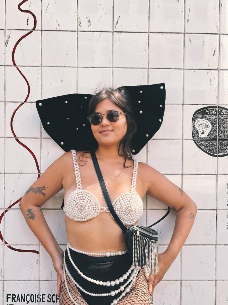 Mulher de pele clara usando top de pérolas, hot pant preta e body chaim 