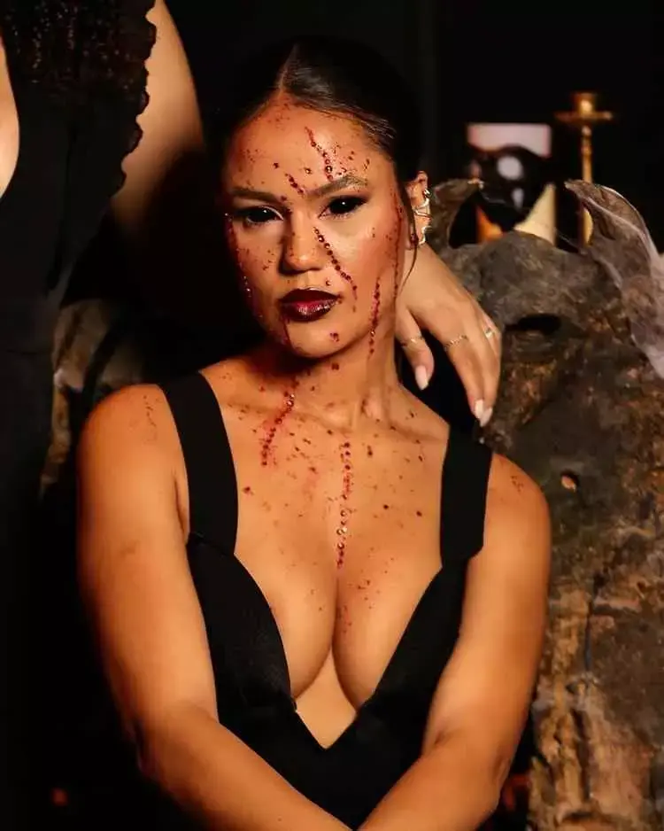 Mulher de pele clara com maquiagem de halloween com pedrarias vermelhas pelo rosto e lente preta