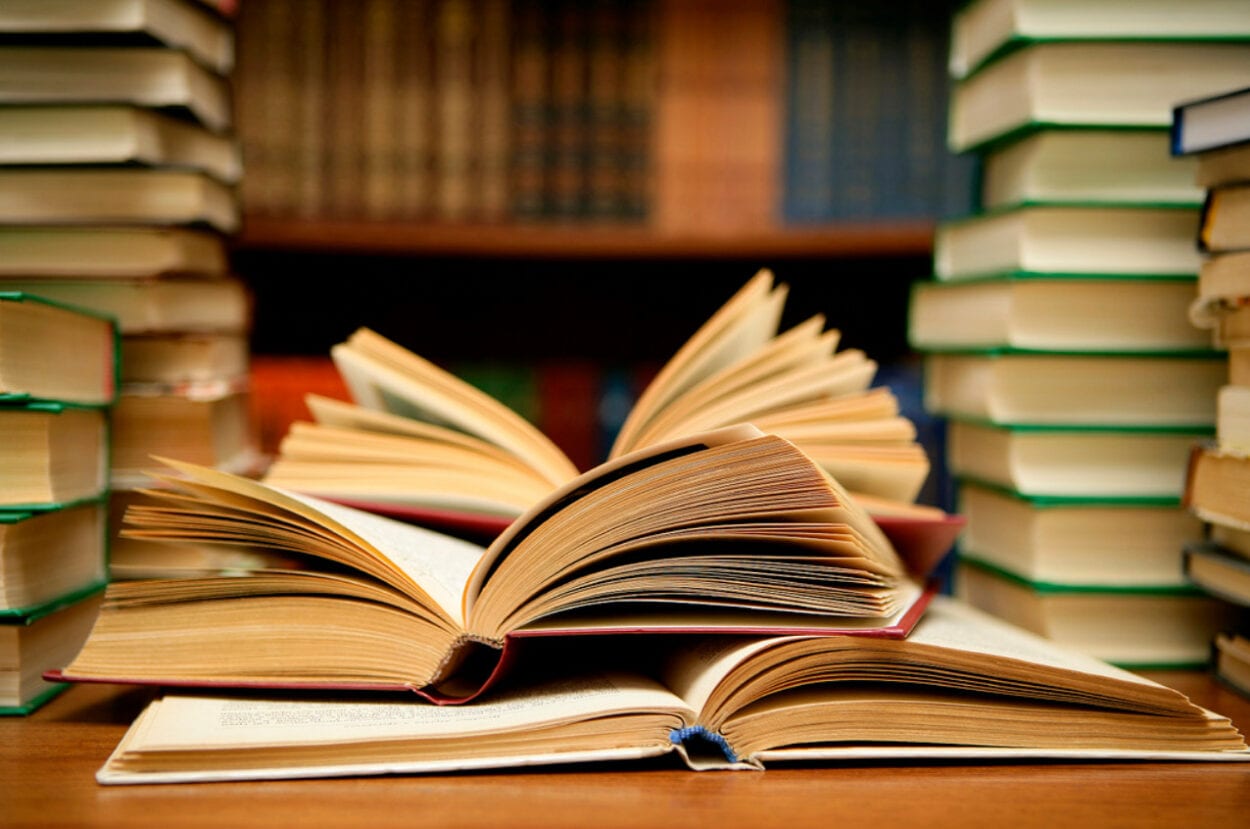 Foto de livros empilhados e alguns abertos sobre mesa marrom