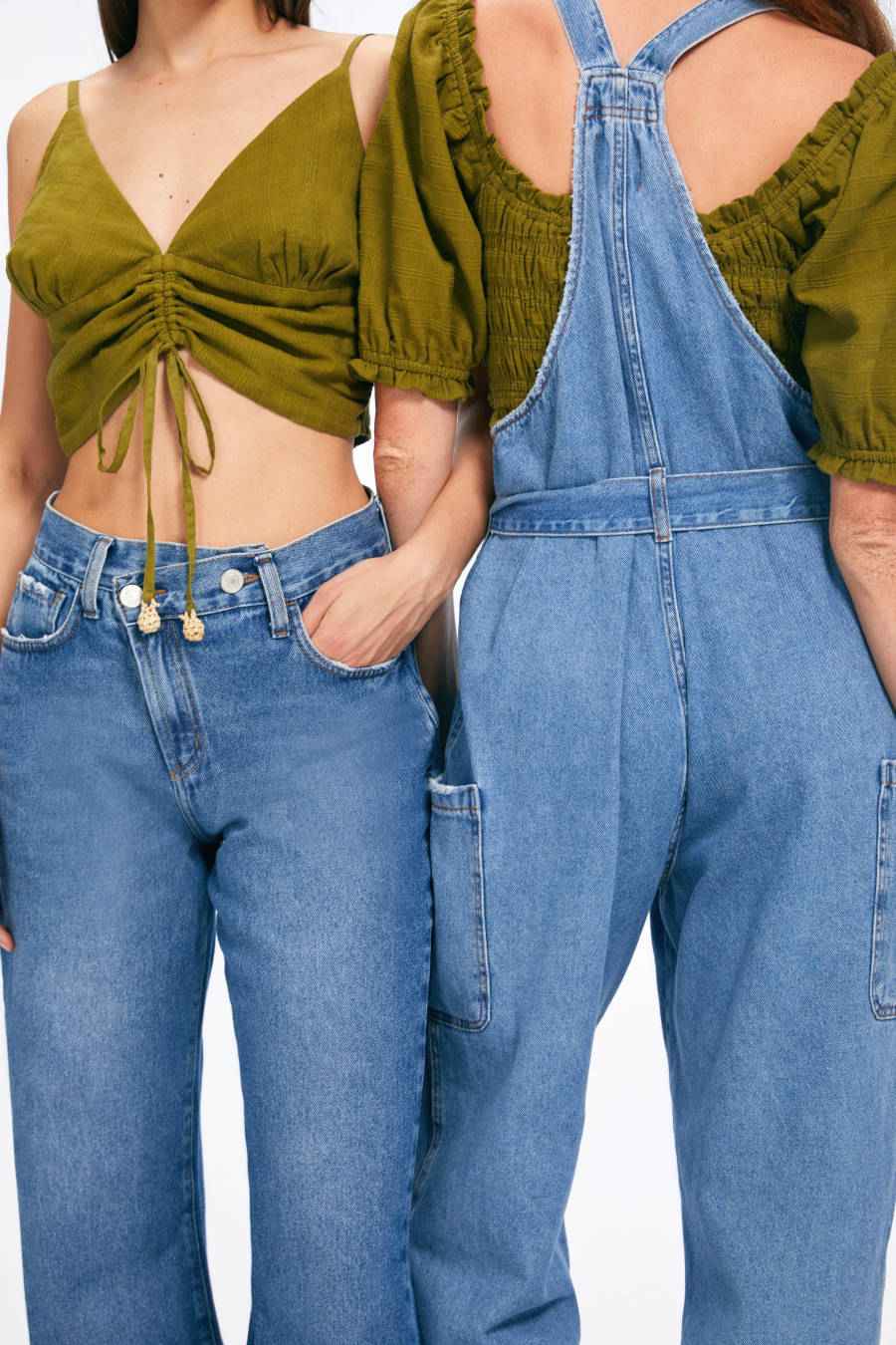 Imagem de duas mulheres usando looks compostos por blusa verde musgo e peças em jeans, uma com calça jeans e outra com macacão jeans