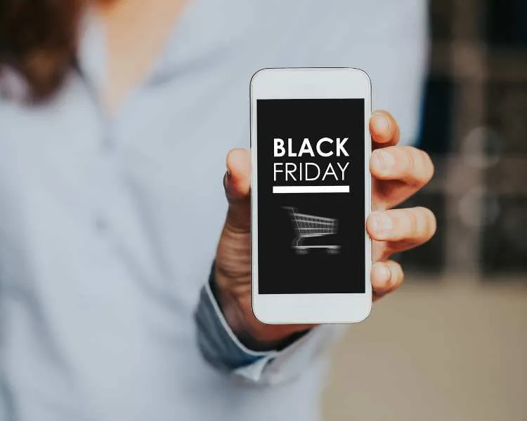 Mão segurando celular que tem escrito de branco em fundo preto "Black Friday" e desenho de um carrinho