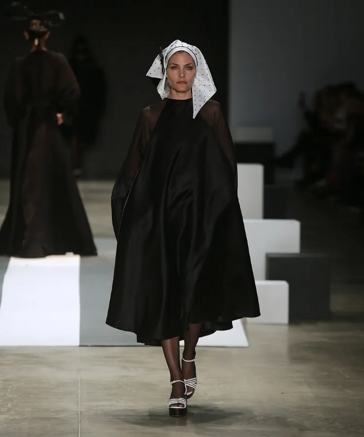 Foto de modelo na passarela usando vestido mídi preto e lenço branco na cabeça