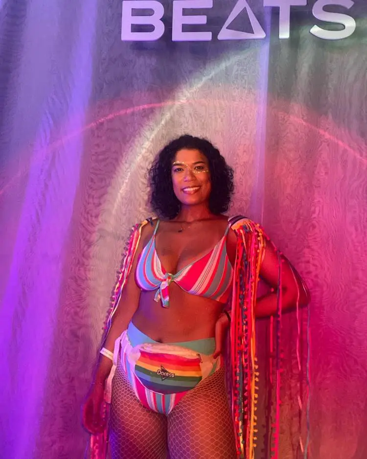 Mulher de pele morena com biquini rosa e azul e fitas coloridas em ombreira 