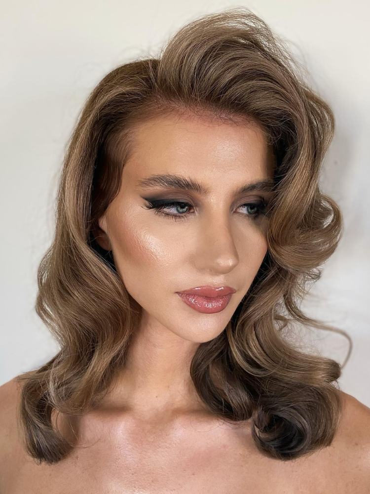 Mulher de pele clara com cabelo loiro escuro ondulado, pele iluminada, delineado esfumado 