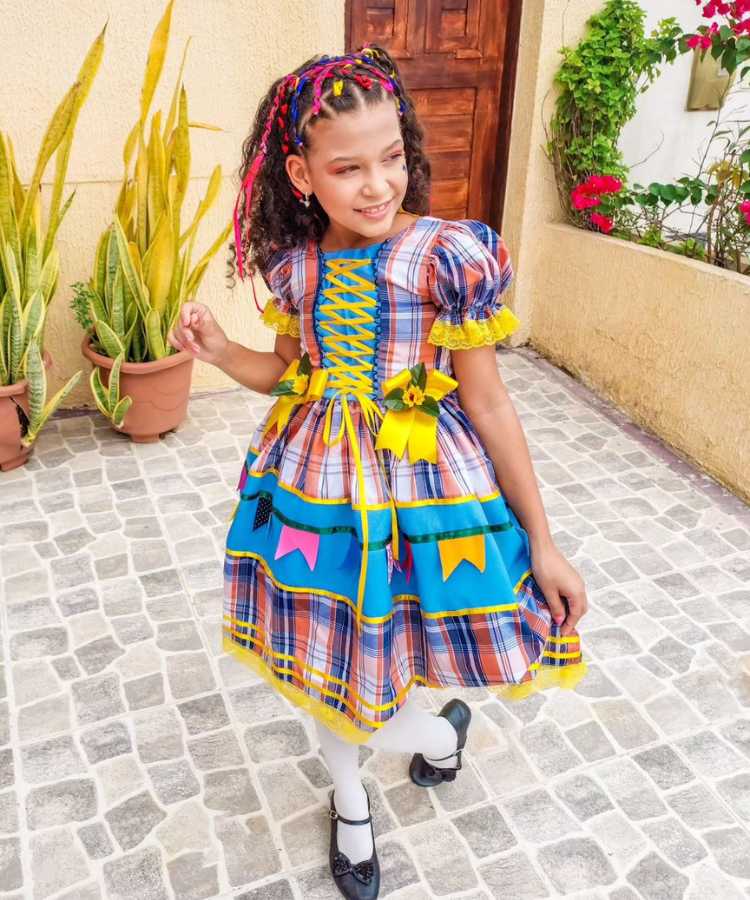 Menina usando vestido xadrez de quadrilha, com girassóis e bandeirinhas