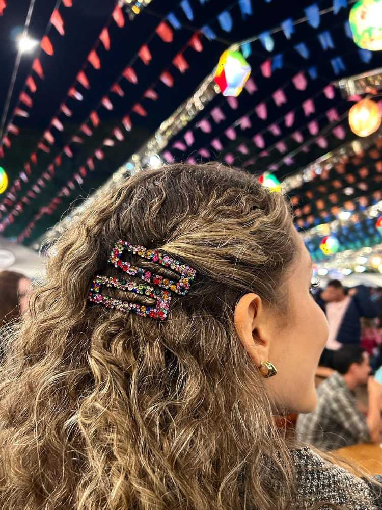 Mulher de pele clara e cabelo cacheado de costas em festa junina usando presilhas coloridas