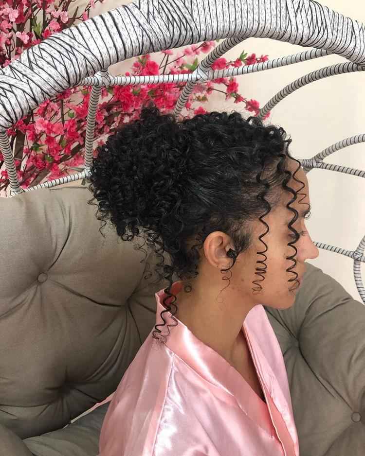 Mulher com coque alto despojado em cabelo preto cacheado