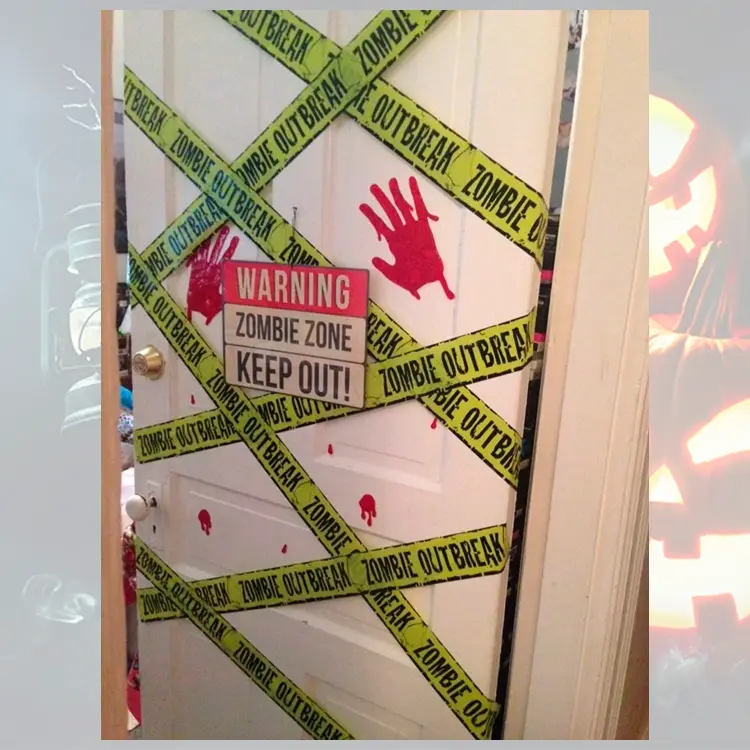 Foto de decoração de porta branca para o Halloween, com fita verde escrito "zombie out break", placa de perigo e marcas de mãos vermelhas 