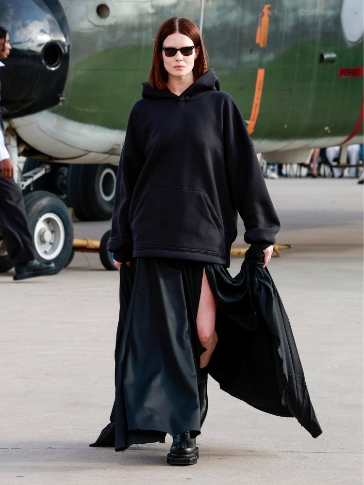 Foto de modelo usando moletom e saia assimétrica pretos em desfile da FORCA Studio no SPFW N60 no Campo de Marte