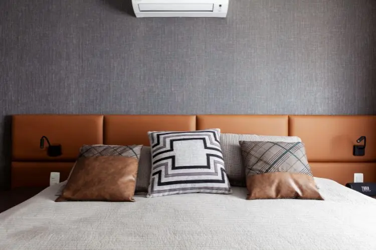 Quarto com parede cinza, ar condicionado, cabeceira em couro marrom e almofadas