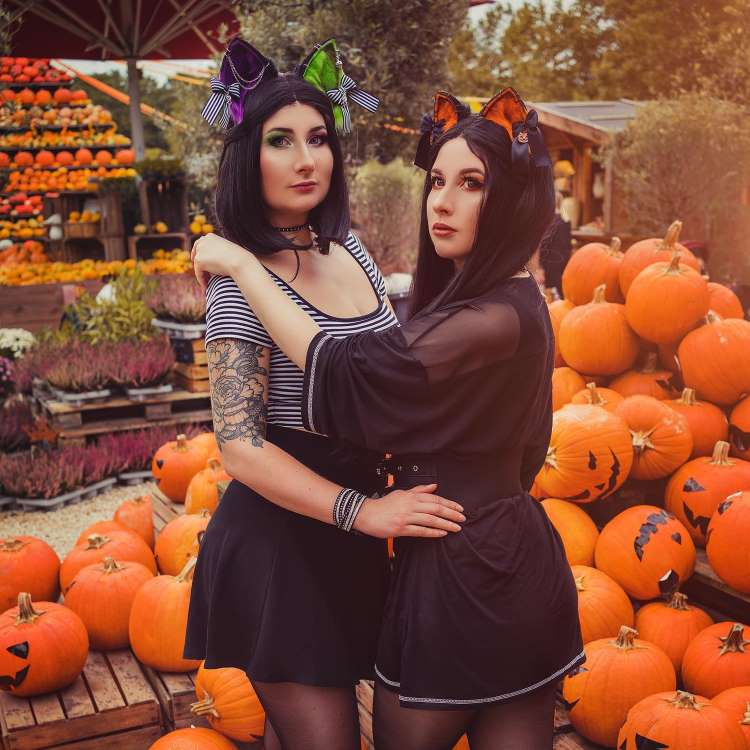 Duas meninas abraçadas, usando tiara de orelha de gato, fantasiadas para o Halloween, em cenário com abóboras