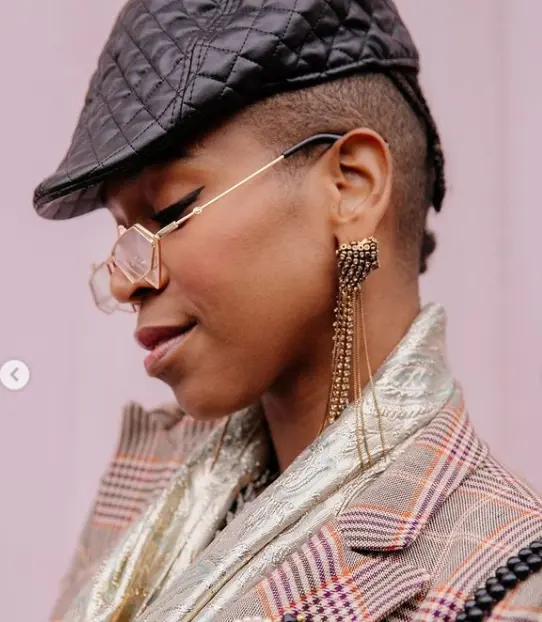 Karol Conka usa boina, blazer xadrez e óculos com lente sobreposta
