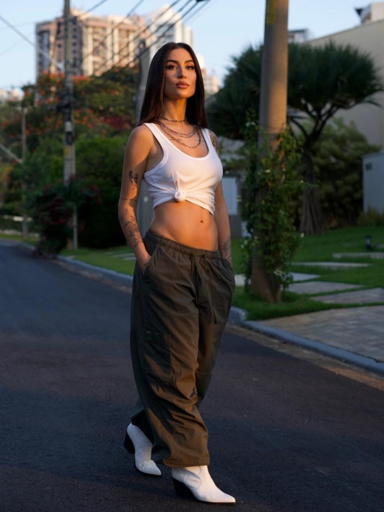 mulher usando regata branca amarrada com um nó, usando calça cargo e uma bota de bico fino branca