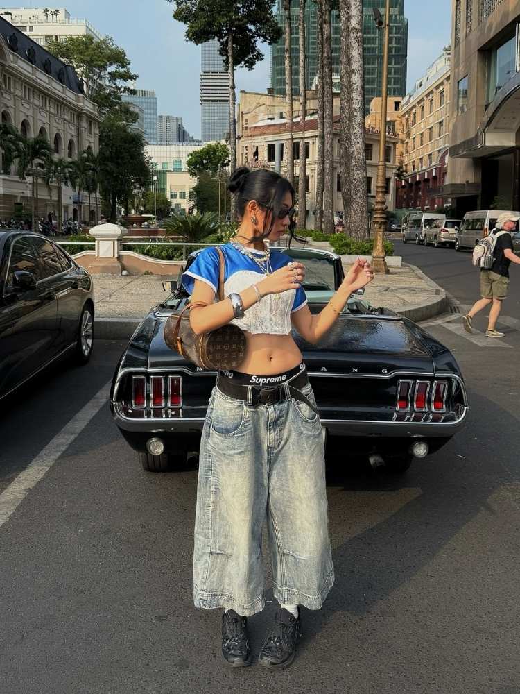 Mulher de pele clara usando blusa azul, corset branco por cima, jorts, calcinha com cós aparecendo, tênis, acessórios 