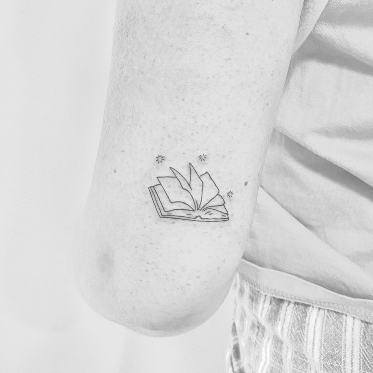 Tatuagem em fineline de livro aberto com brilhos 