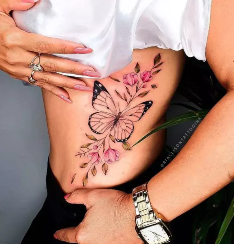 Tatuagem grande de borboleta na costela com flores em rosa 