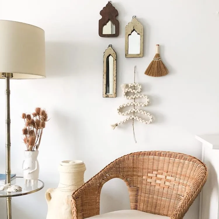 Canto de sala com abajur, cadeira de palha, vaso e na parede 3 espelhos emoldurados, decoração de palha e árvore-de-natal minimalista, feita de artesanato