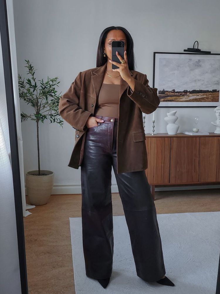 mulher usando blusa marrom, blazer oversized e calça wide leg de couro com scarpin preto
