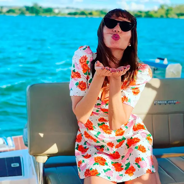 Maria em barco usando vestido floral e mandando beijo