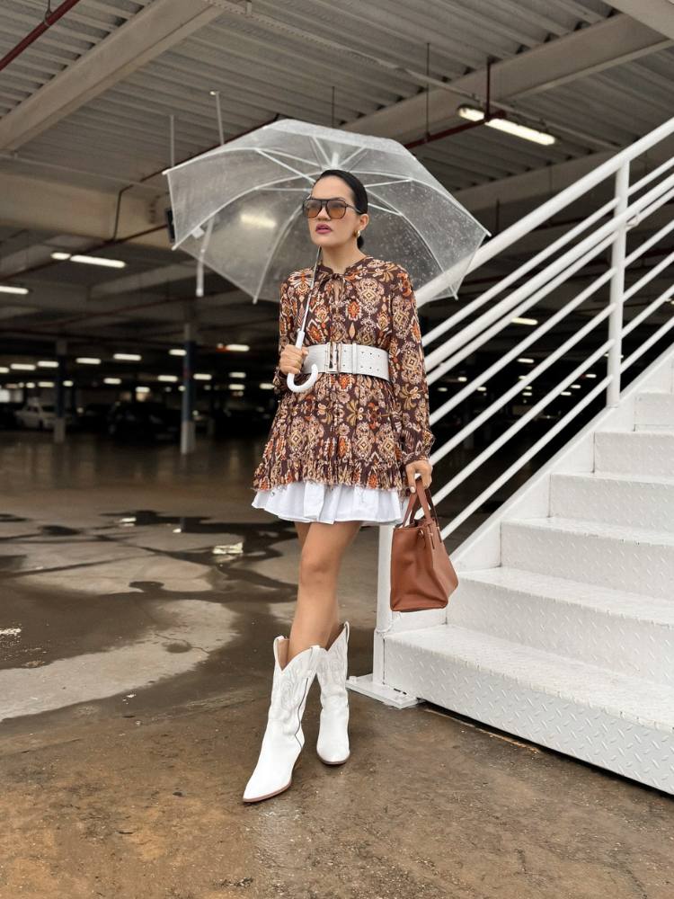 Mulher de pele clara usando camisa boho, saia branca, bota western branca e guarda-chuva 