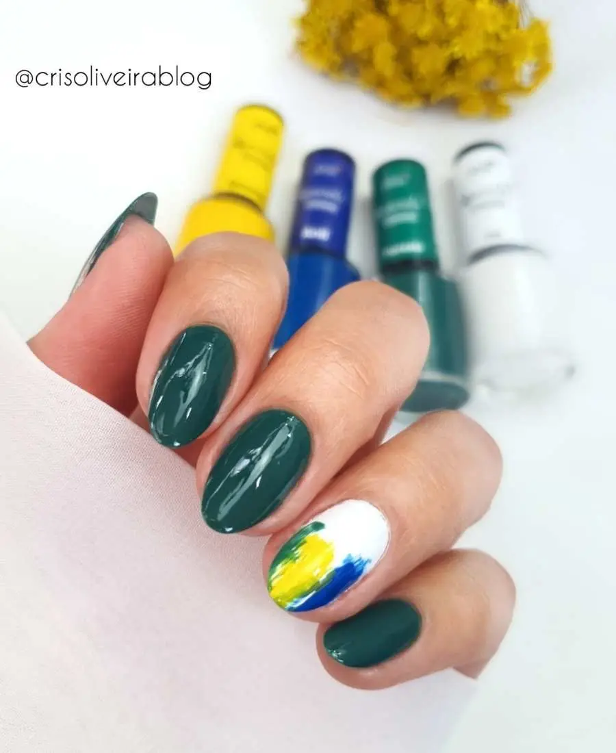 Imagem de mão com unhas decoradas para a Copa do Mundo 2022. Cores usadas, verde, amarelo, azul e branco. Polegar, indicado, médio e mínimo, verde. Anelar, branco com verde, amarelo e azul.